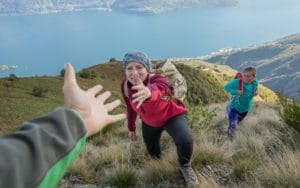 Three people hiking up a mountain path with first person stretching out a hand to help the second