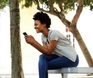 Woman sitting on a bench outside while checking texts on mobile phone