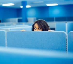 Woman peeking over a blue cubicle wall